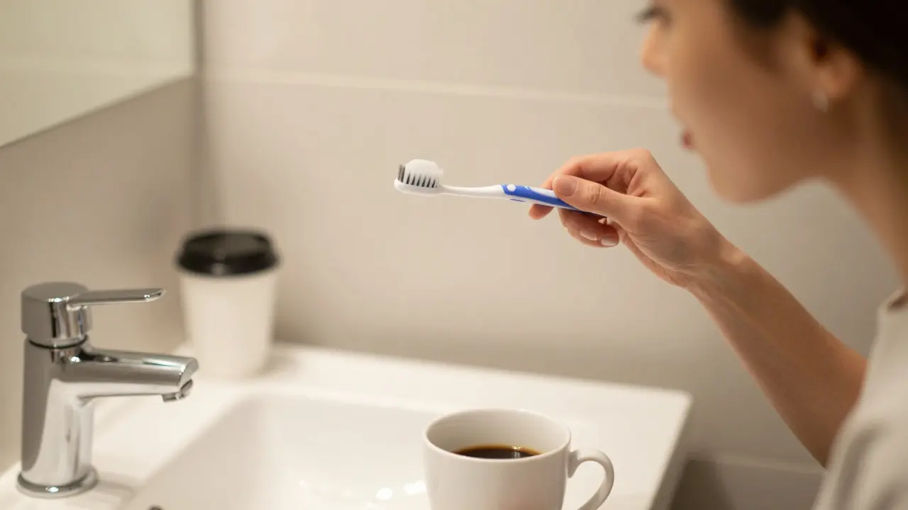 Grafik čistí zuby měkkým kartáčkem s kávou na umyvadle, fazety jsou viditelné.